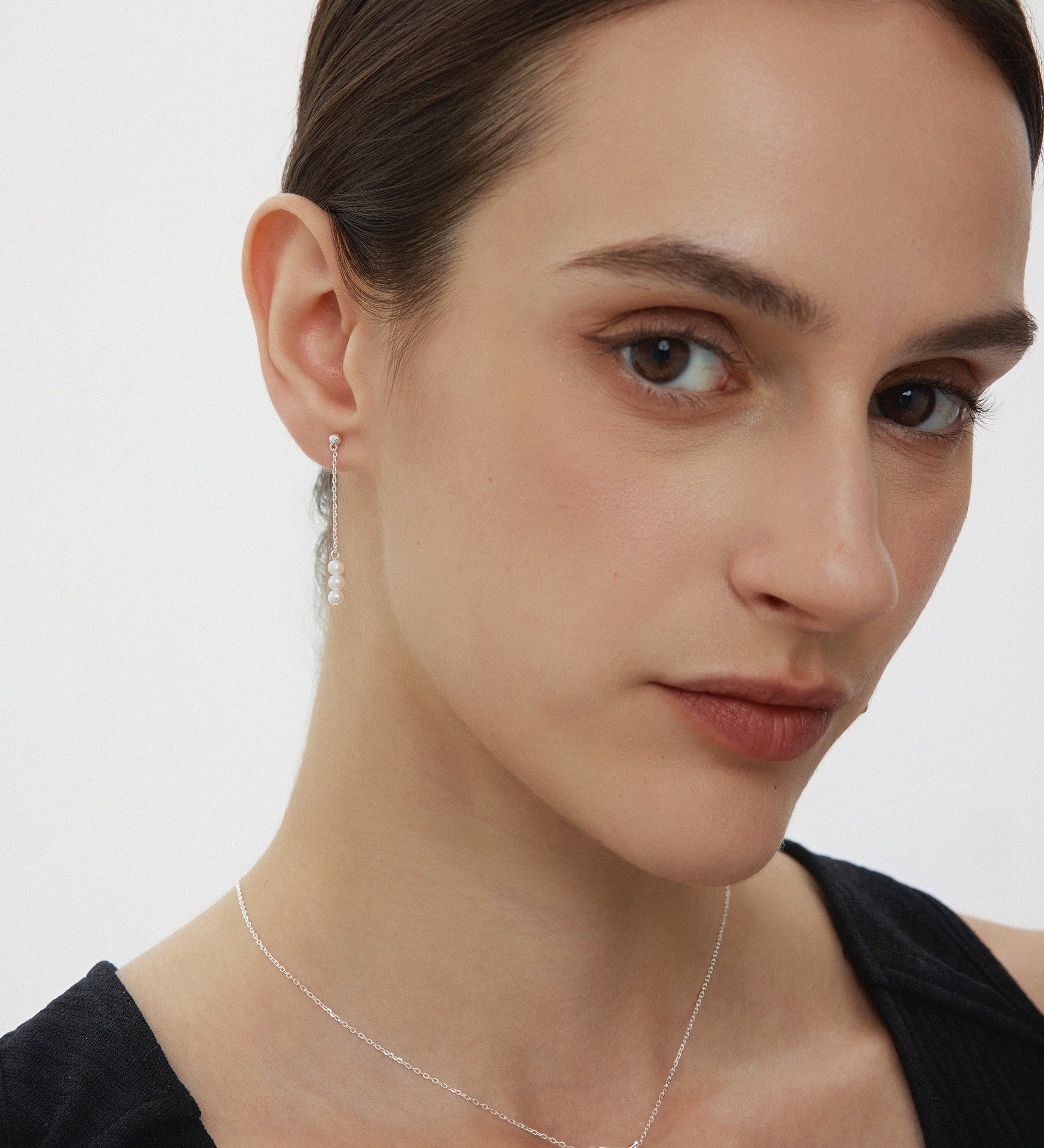 Woman wearing a delicate necklace with a silver pendant on a plain background