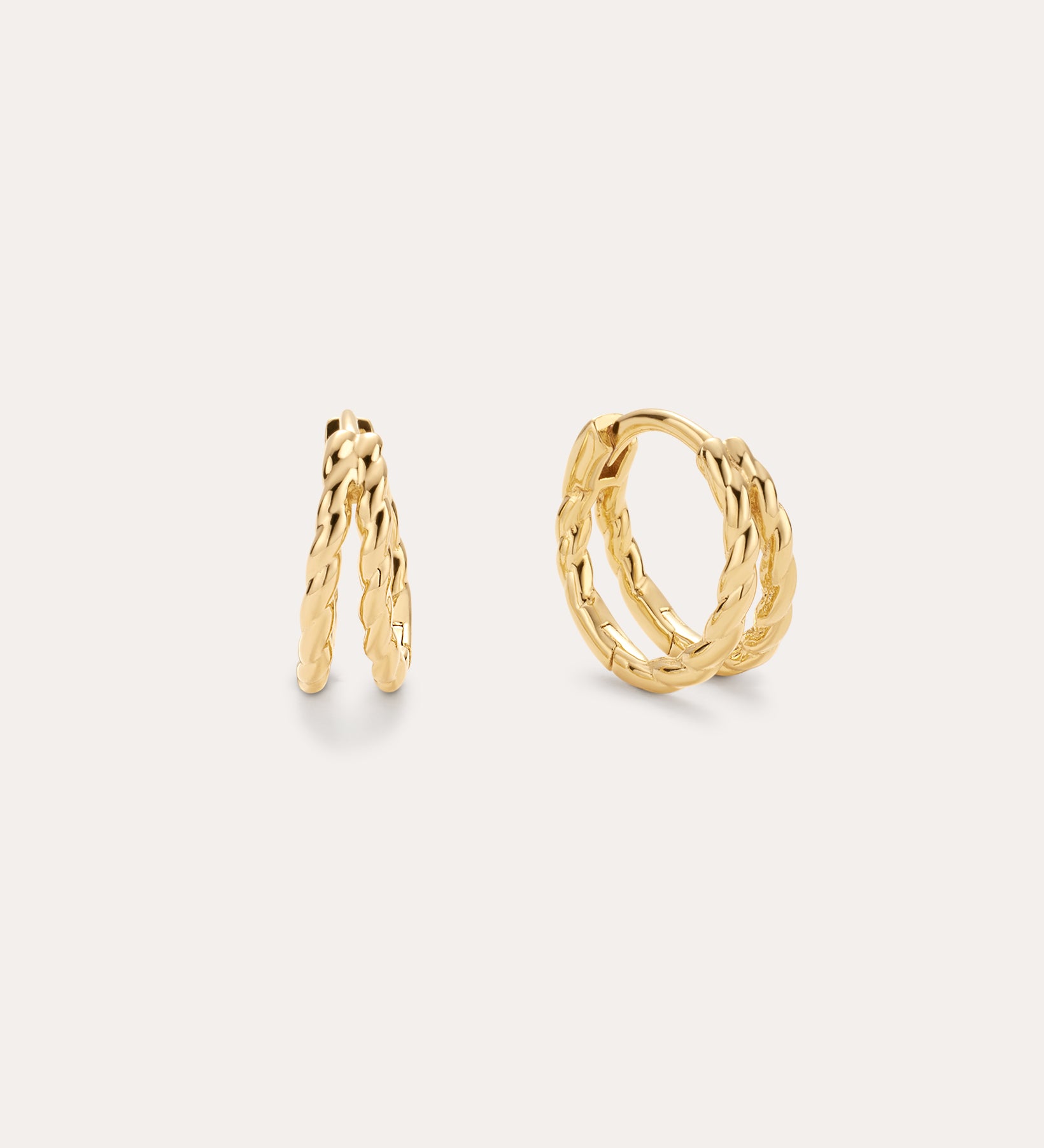 The Mae Twist Double Huggie Earrings in Gold, featuring a delicate twisted rope design, are displayed against a plain, light background.