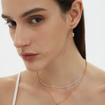 A woman with straight brown hair wears gold jewelry, including the Crescent Moon Crystal Charm Beaded Necklace in Gold. She is dressed in a white spaghetti strap top against a plain background.