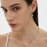 A woman with straight brown hair wears gold jewelry, including the Crescent Moon Crystal Charm Beaded Necklace in Gold. She is dressed in a white spaghetti strap top against a plain background.