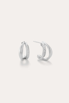 Nadine Pavé Twisted Stud Earrings in Silver feature lightweight, asymmetrical silver hoops with a row of sparkling stones along the inner curve, displayed on a plain white background.