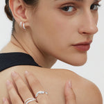 A woman with slicked-back hair wears a sleeveless black top, silver hoop earrings, and the Noor Pavé Triple Band Ring in Silver as she looks over her shoulder at the camera against a plain white background.