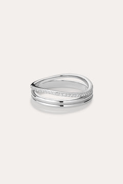 The Noor Pavé Triple Band Ring in Silver showcases a modern overlapping design with a polished finish and a row of sparkling pavé diamonds along one edge, elegantly set against a light background.
