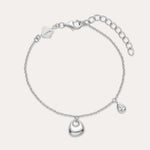 The Nora Double Pendant Bracelet in Silver features a polished heart charm at the center and a small teardrop pendant, both accented with cubic zirconia, plus an adjustable clasp and logo tag near the fastening.