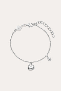 The Nora Double Pendant Bracelet in Silver features a polished heart charm at the center and a small teardrop pendant, both accented with cubic zirconia, plus an adjustable clasp and logo tag near the fastening.