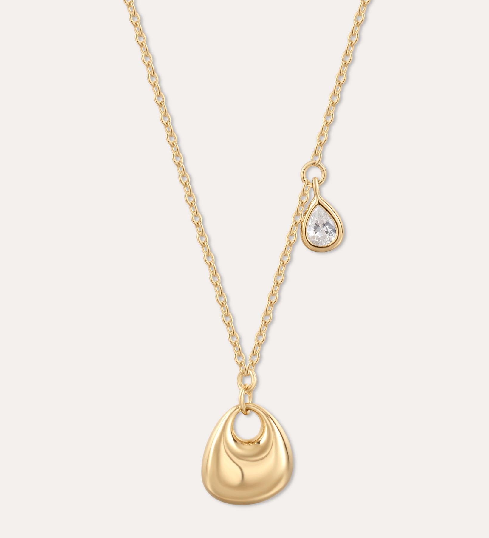 The Nora Double Pendant Necklace in Gold features a smooth sculptural pendant and a delicate teardrop charm with clear cubic zirconia, displayed on a plain light background.