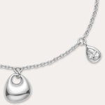 The Nora Double Pendant Bracelet in Silver features an adjustable clasp, a small heart-shaped charm, and a tiny cubic zirconia teardrop charm dangling side by side.