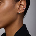 Close-up of a person’s ear wearing Ribbon Twist Huggies in Silver on the lobe and another silver huggie on the upper ear. The person has smooth skin and is dressed in a black blazer.
