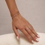 A manicured hand rests on a soft white surface, adorned with a delicate silver bracelet, a sterling silver ring, and the Bamboo Chunky Crystal Ring in Silver.