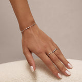 A manicured hand rests on a soft white surface, adorned with a delicate silver bracelet, a sterling silver ring, and the Bamboo Chunky Crystal Ring in Silver.