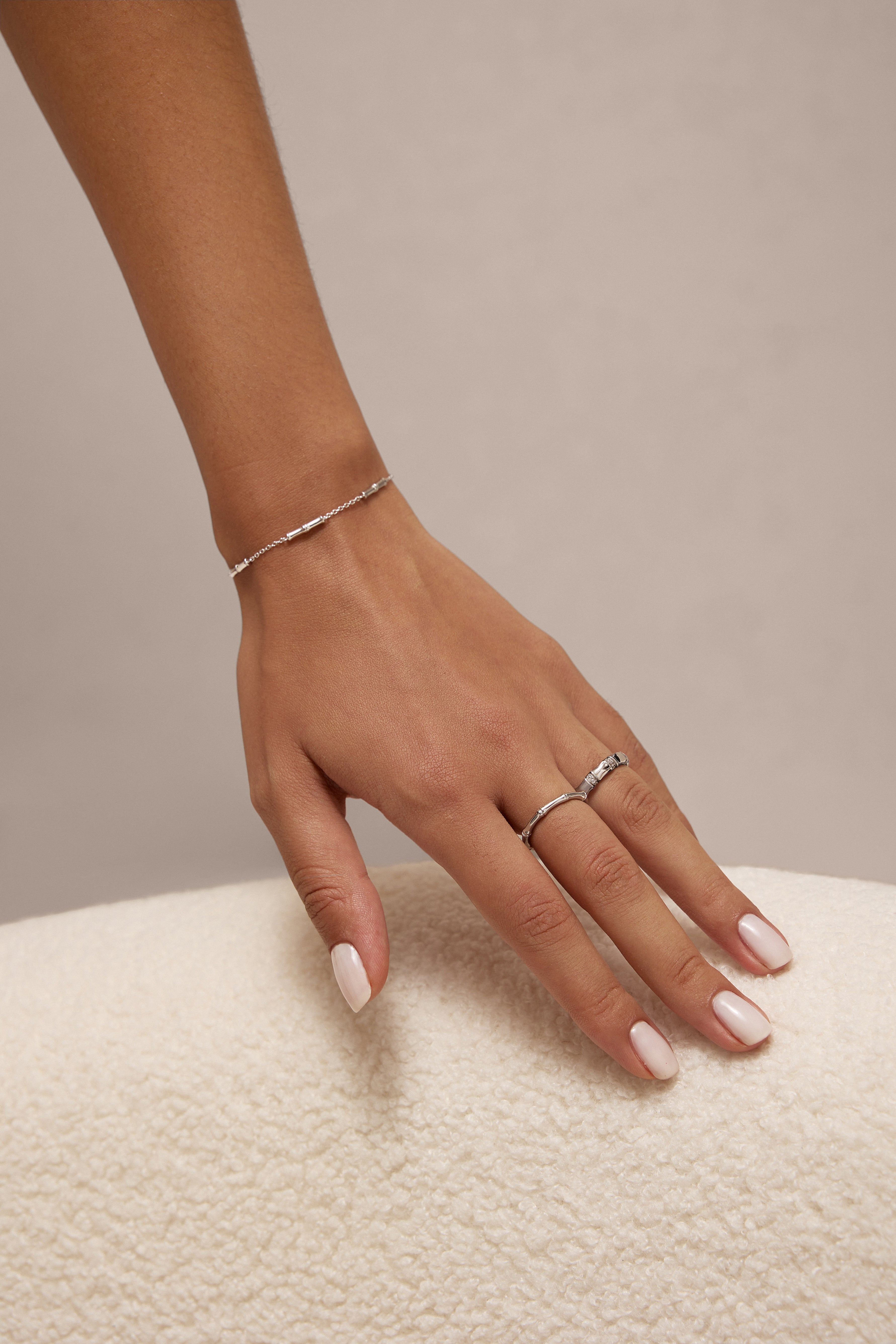 A manicured hand rests on a soft white surface, adorned with a delicate silver bracelet, a sterling silver ring, and the Bamboo Chunky Crystal Ring in Silver.