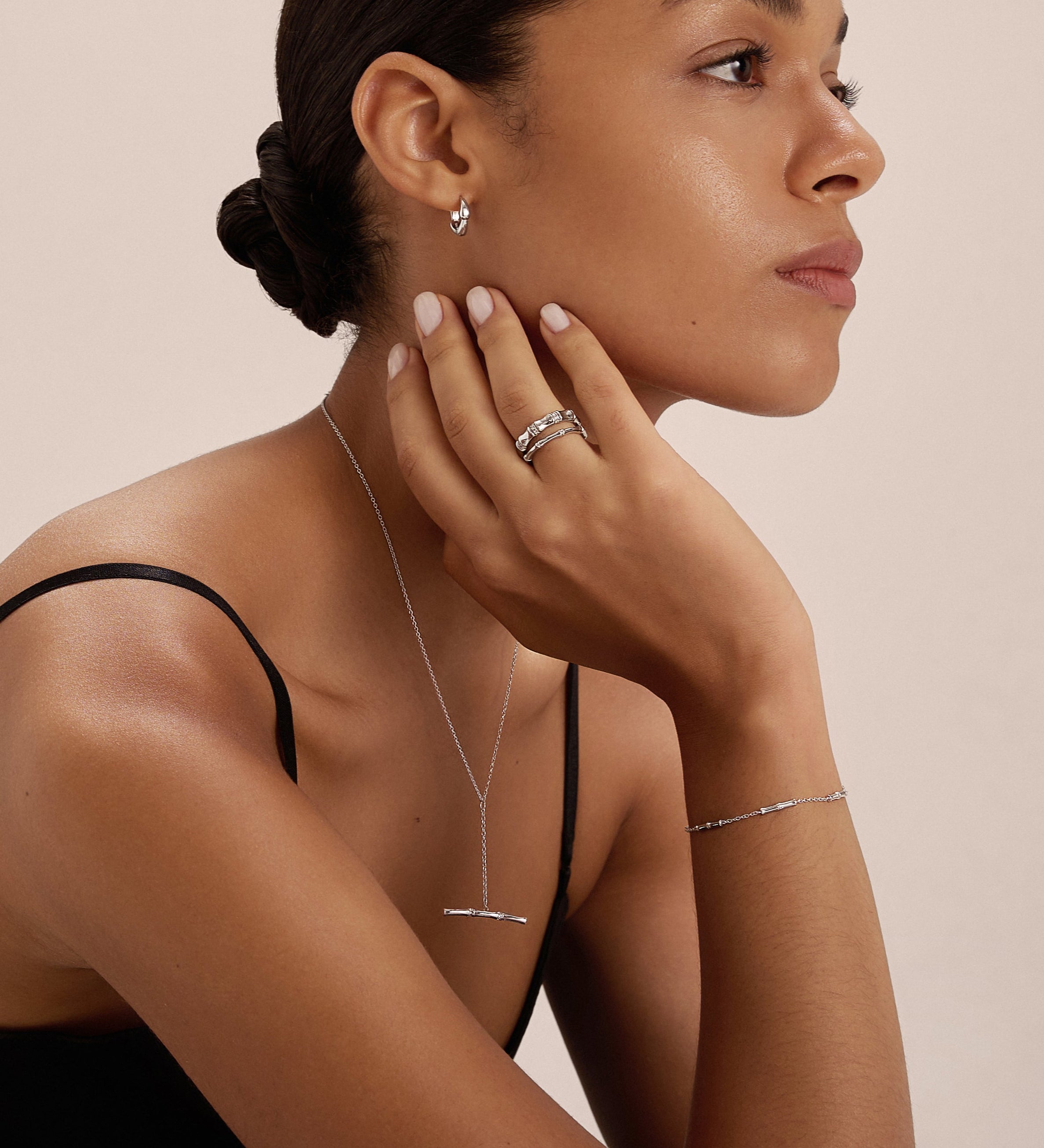 A woman with slicked-back hair wears a black sleeveless top and minimal jewelry, including the Bamboo Ring in Silver, as she thoughtfully poses with her hand on her chin against a plain background.