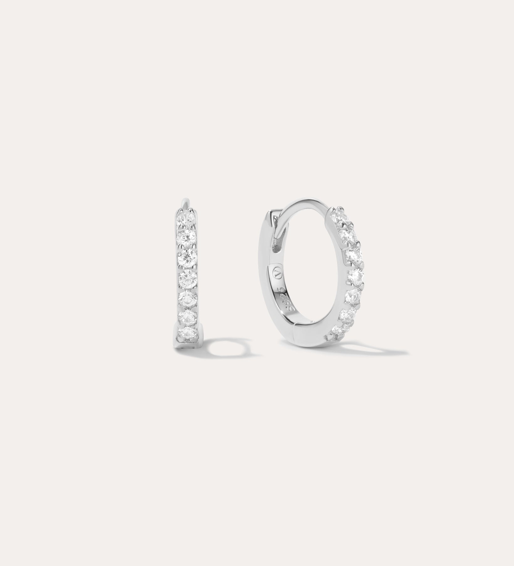 The Kiki Crystal Huggie Earrings in Sterling Silver feature a sparkling row of white gemstones. Shown facing forward and from the side, they are versatile everyday essentials for any ear piercing.