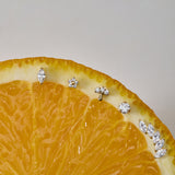A close-up of a sliced orange displays the Marquise Threadless Flat Back Titanium Cartilage Stud in Gold, along with other sparkling gemstone earrings, arranged along the curved edge against a neutral background.