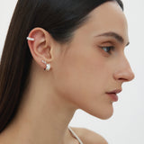 A woman with straight dark hair wears the Vera Twisted Crystal Ear Cuff in Silver on her upper ear, along with a small silver hoop in her lobe. She has natural makeup and is dressed in a white thin-strapped top.