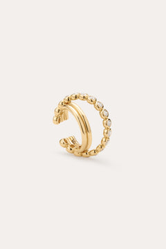 The Vina Crystal Bezel Ear Cuff in Gold features a beaded design with small, round clear cubic zirconia along the outer edge, shown on a light beige background.