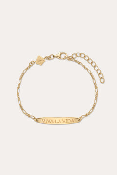 The Viva La Vida Bar Chain Bracelet in Gold features an adjustable clasp, a rectangular plate engraved with VIVA LA VIDA, and a small hexagonal charm near the clasp. Inspired by the classic Viva La Vida necklace; shown on a light beige background.